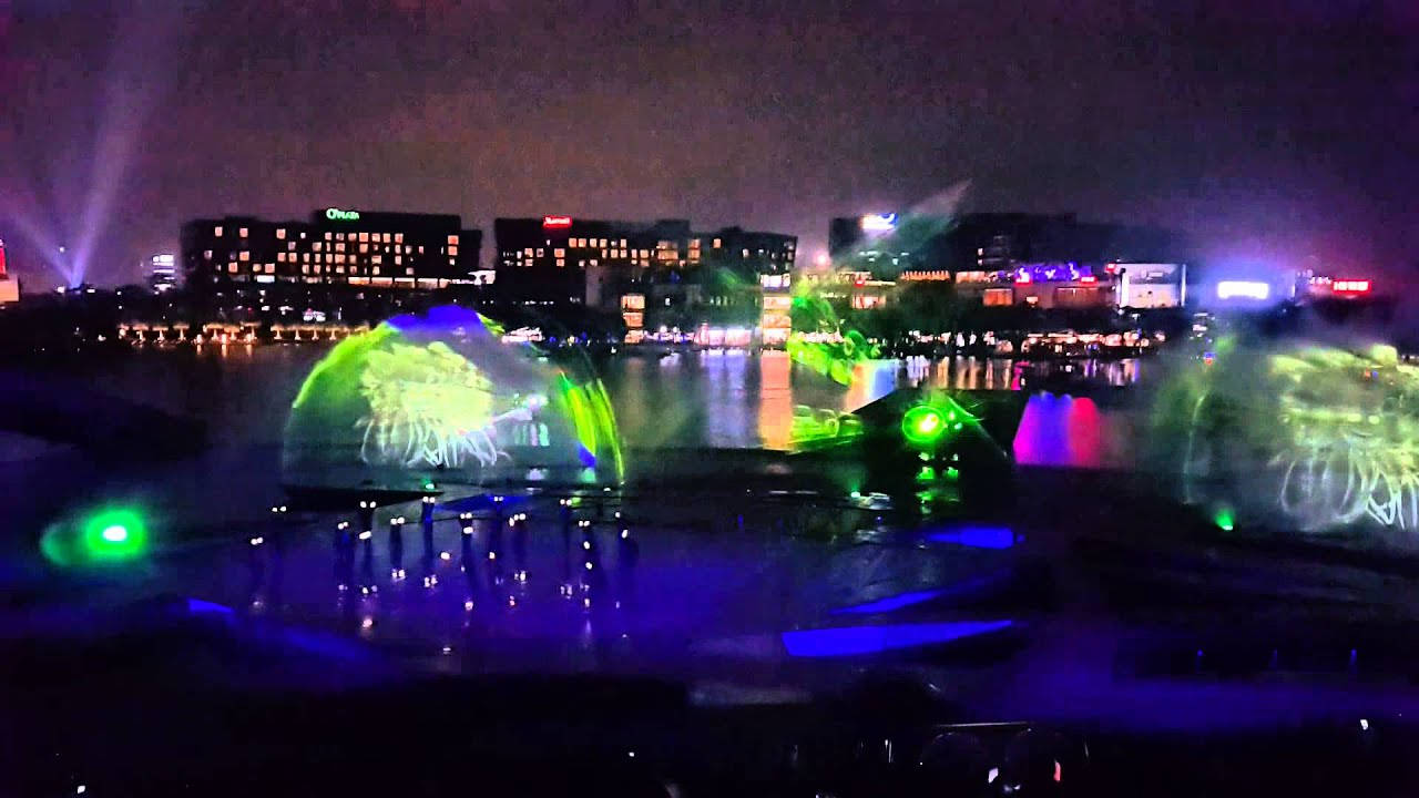 深圳水舞秀 壁紙 — 一場令人眼花繚亂的夜間水舞表演，霓虹綠和藍色燈光投射在舞動的噴泉上，映襯著城市天際線。