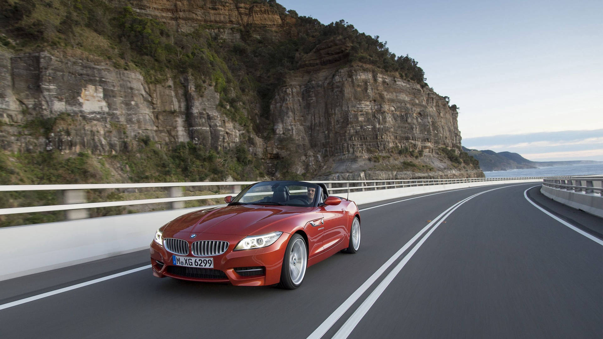 紅色BMW Z4開篷跑車在海岸公路上行駛，懸崖和海洋