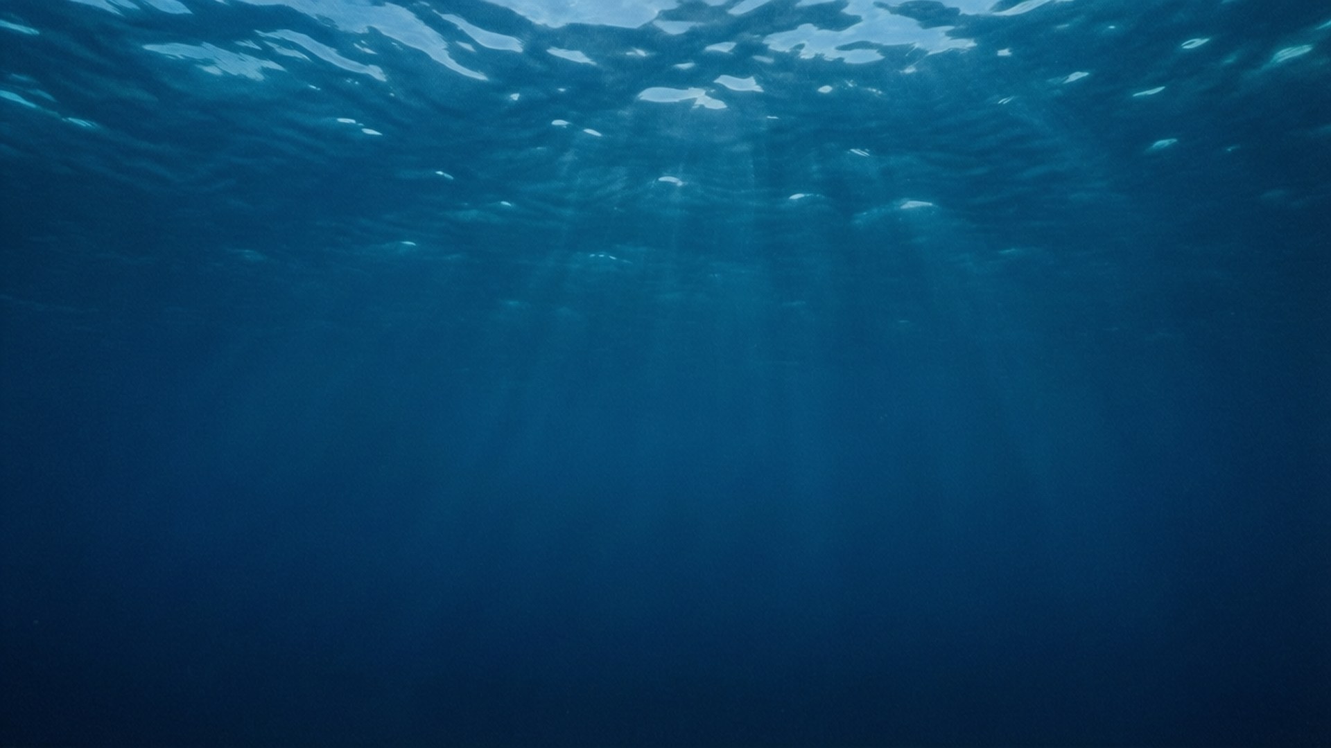 深海之境 壁紙 — 陽光穿透漣漪的海面，在深藍色海水中投射出空靈的光線。