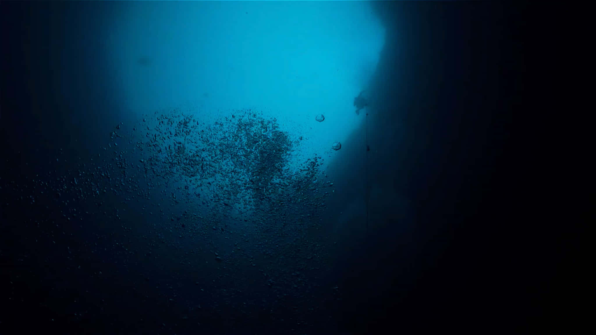 深海幽谷的陰森水下場景 壁紙 — 一名潛水員的剪影穿過碧綠色的海水上升，向著上方明亮的水面釋放氣泡。