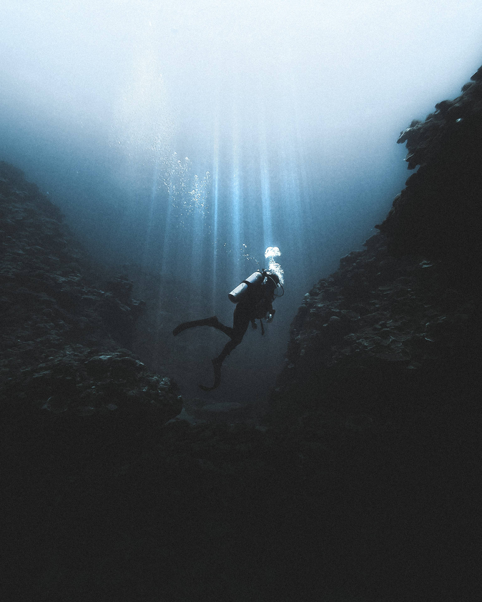 深海潛水員 GoPro 壁紙 — 一名潛水員在狹窄的水下峽谷中滑行，陽光穿透上方的藍色海水。