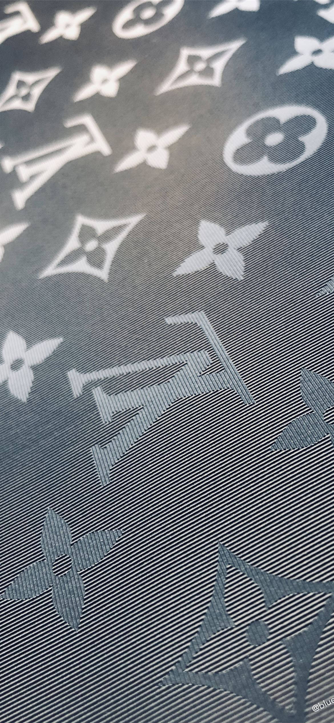 路易威登 桌布 壁紙 — 深灰色布料近距離特寫，帶有重複的白色 Louis Vuitton 字母圖案和花卉圖案。