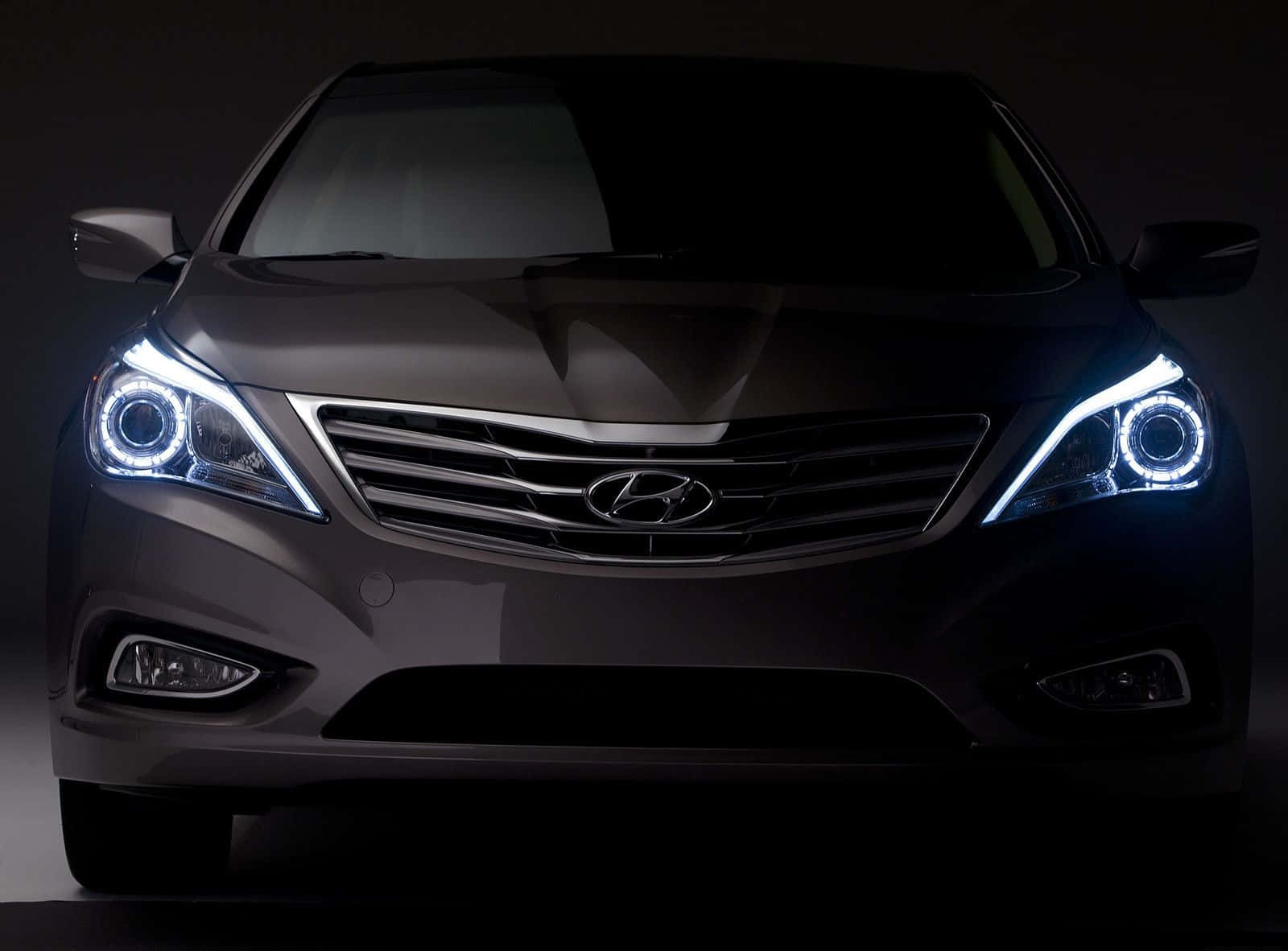 Hyundai Azera 桌布 壁紙 — 深灰色現代房車的正面視圖，帶有發光的藍色光環頭燈，背景為黑色攝影棚。