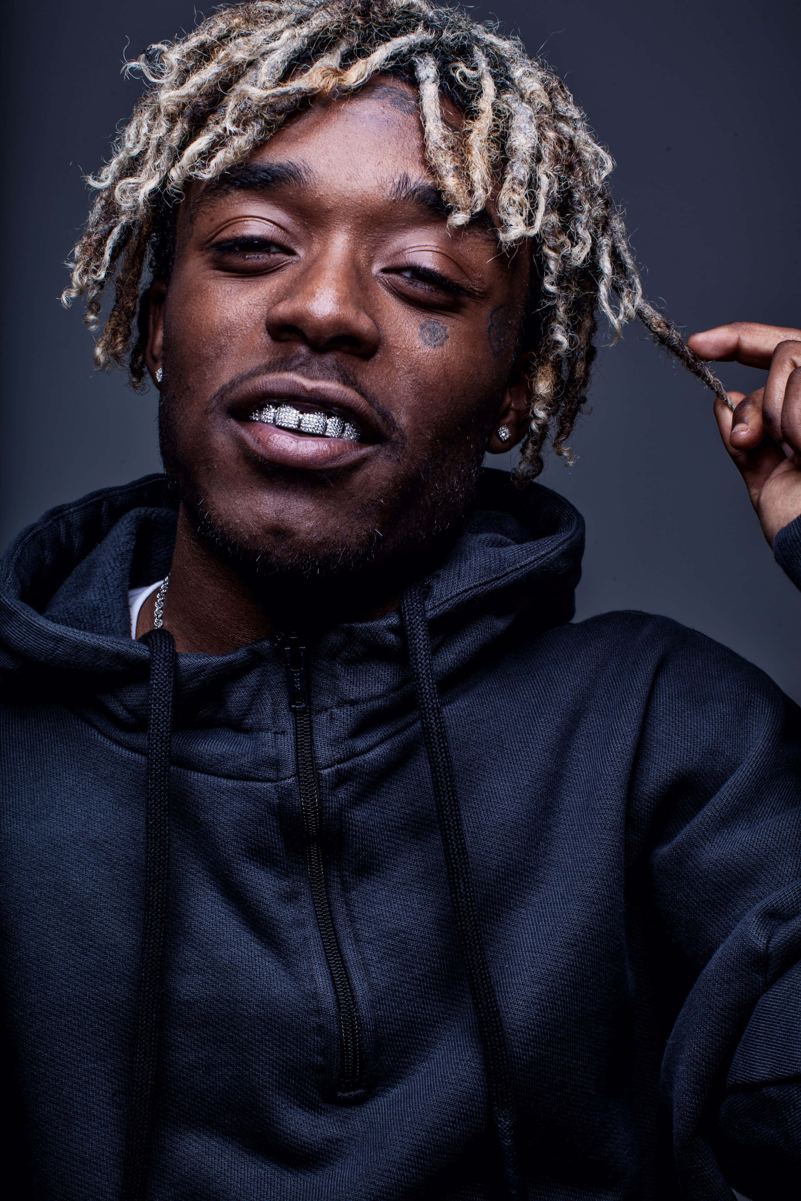 Lil Uzi Vert 桌布 壁紙 — 深灰色背景上，一名擁有金色辮子頭和鑽石牙套的男子特寫肖像。