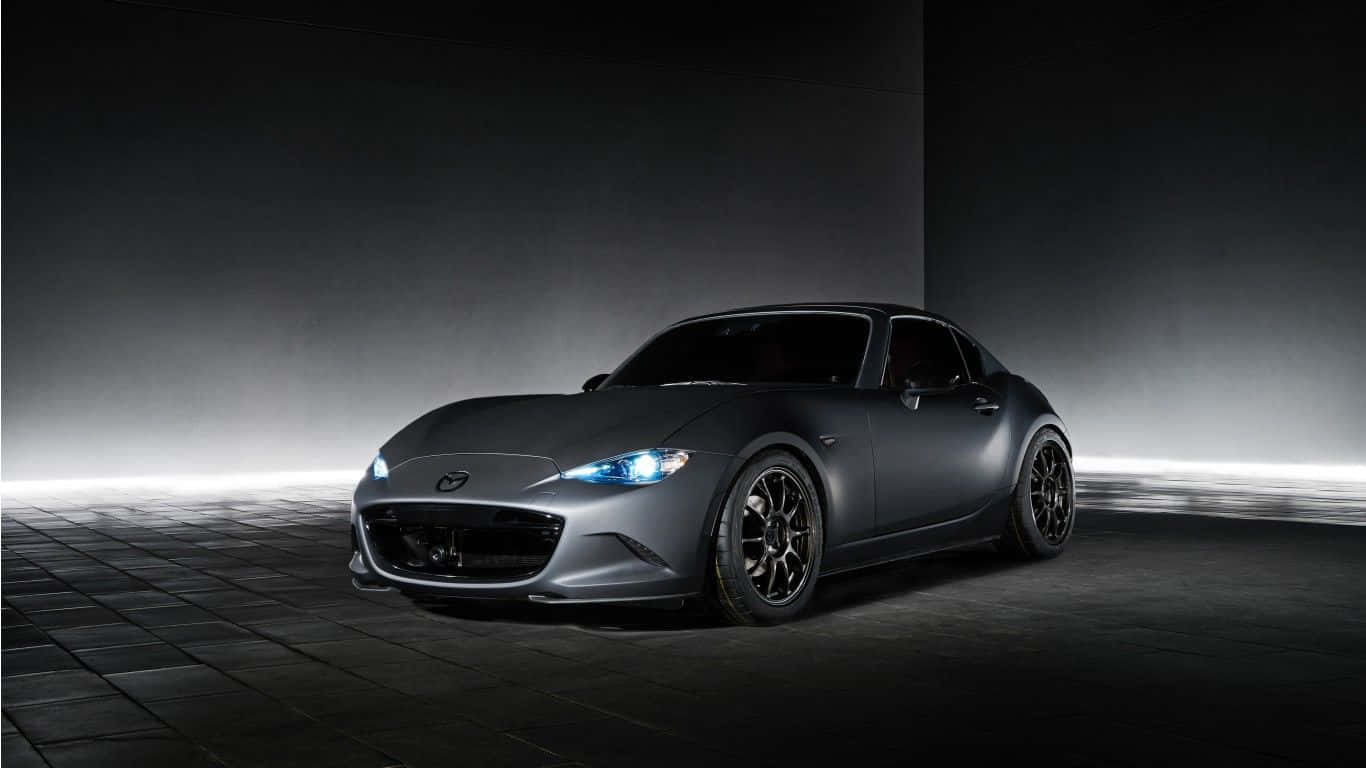 深灰色馬自達MX-5 Miata跑車 壁紙 — 一輛時尚的啞光灰色跑車在戲劇性的工作室燈光下，在瓷磚地板上發出明亮的藍色車頭燈光芒。