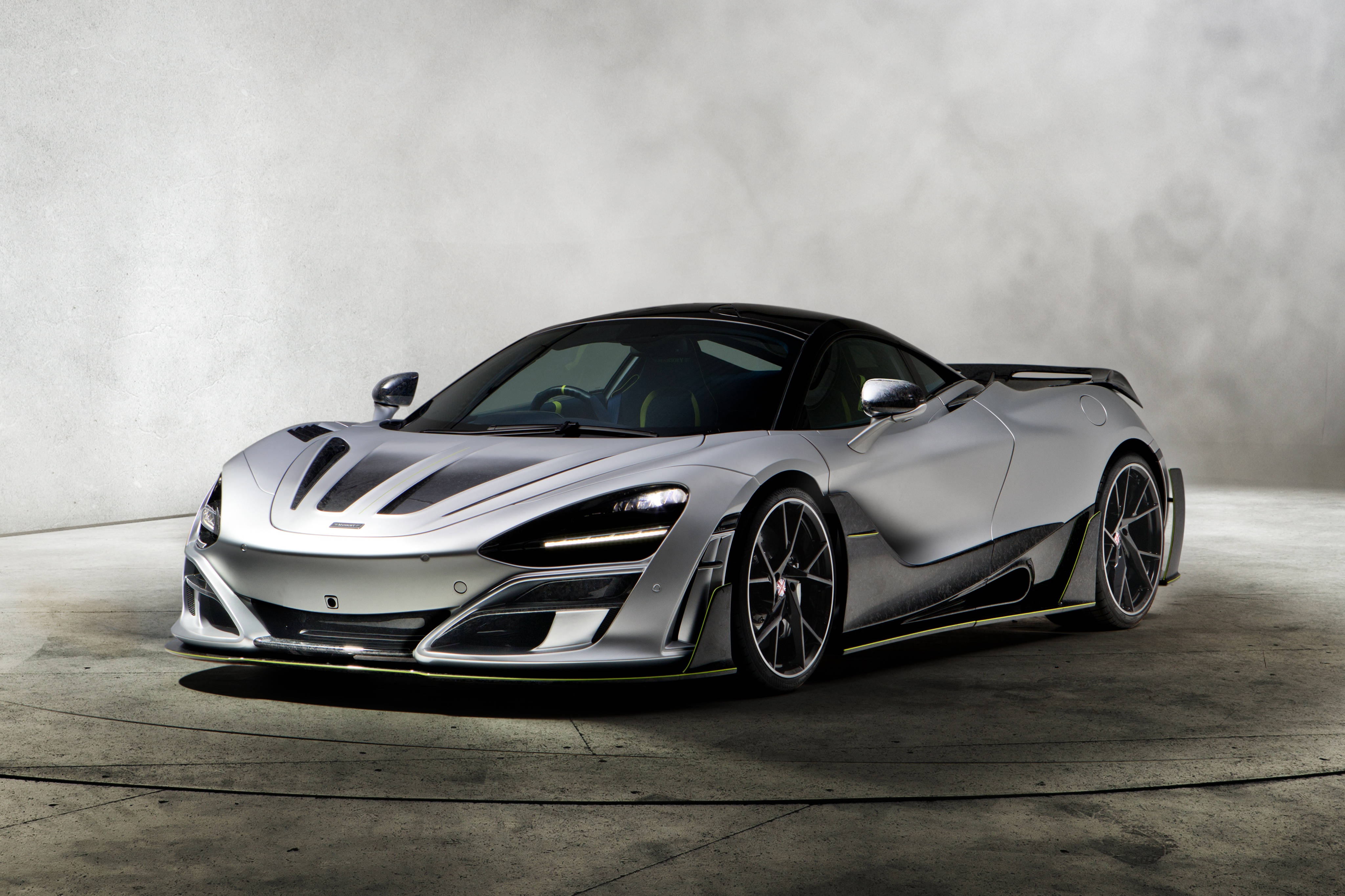 深灰色麥拉倫720S 壁紙 — 一輛時尚的銀色McLaren超級跑車，帶有黑色飾邊和黃色裝飾，在一個極簡主義的工作室中展示，地板是混凝土的，牆壁有紋理。