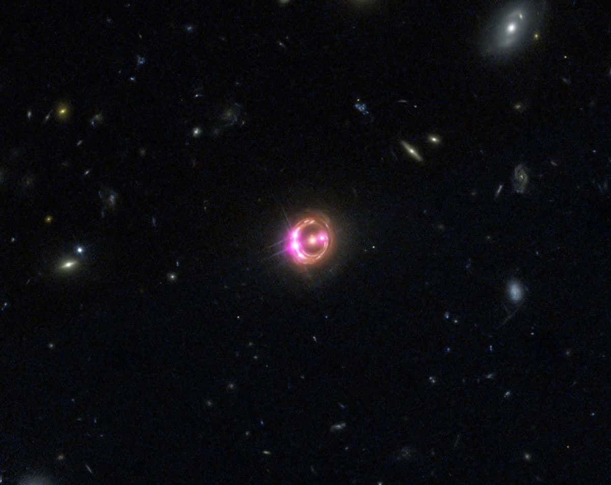 深空中的壯觀類星體 壁紙 — 一顆發光的粉紅色環狀類星體在深空中，以遙遠星系和恆星為背景，明亮地閃耀。
