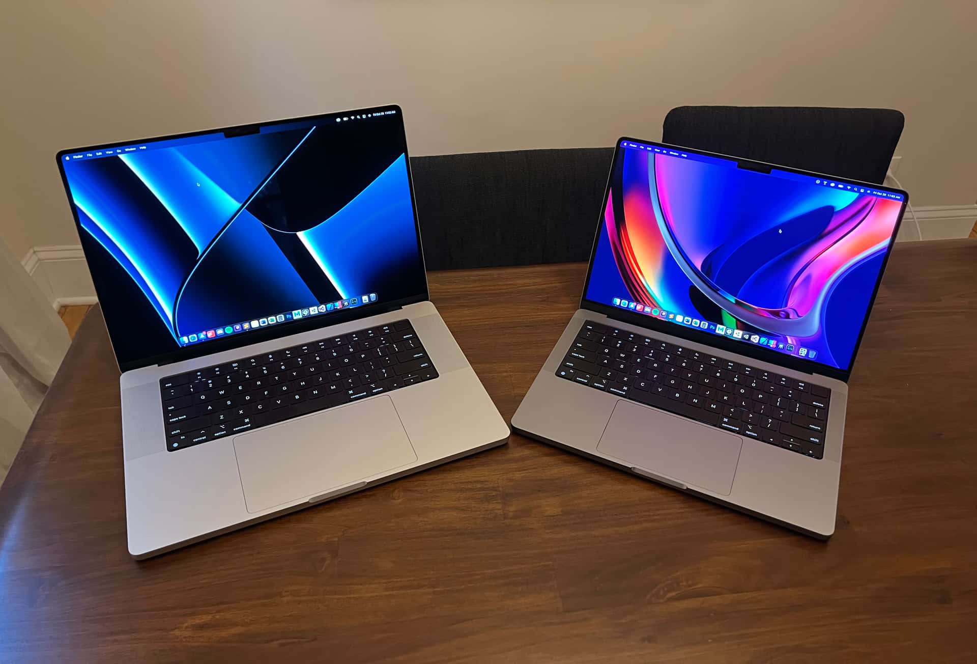 深空灰MacBook靜置於綠色背景前 壁紙 — 兩部銀色手提電腦展示充滿活力的抽象壁紙，打開放在木桌上，房間光線柔和。