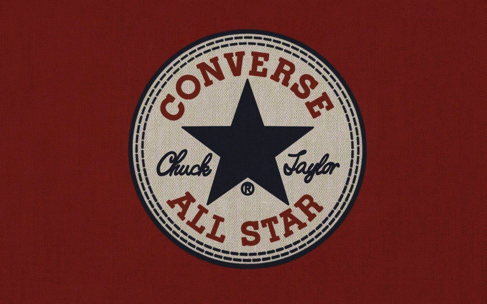 深紅色布料匡威標誌 壁紙 — 經典 Converse All Star 標誌貼片，海軍藍星星和紅色文字，背景為有紋理的深紅色布料。