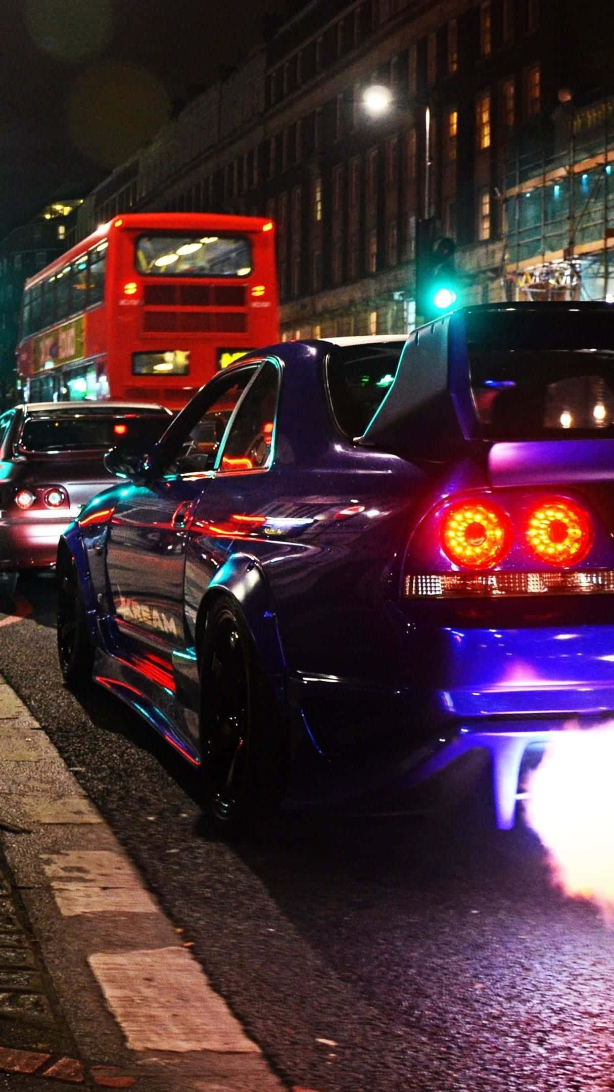 深紫色低調R33 GTR 壁紙 — 一輛閃亮的紫色跑車，帶有發光的橙色尾燈和藍色底盤燈，在夜間濕漉漉的城市街道上行駛，背景中有一輛紅色的雙層巴士。