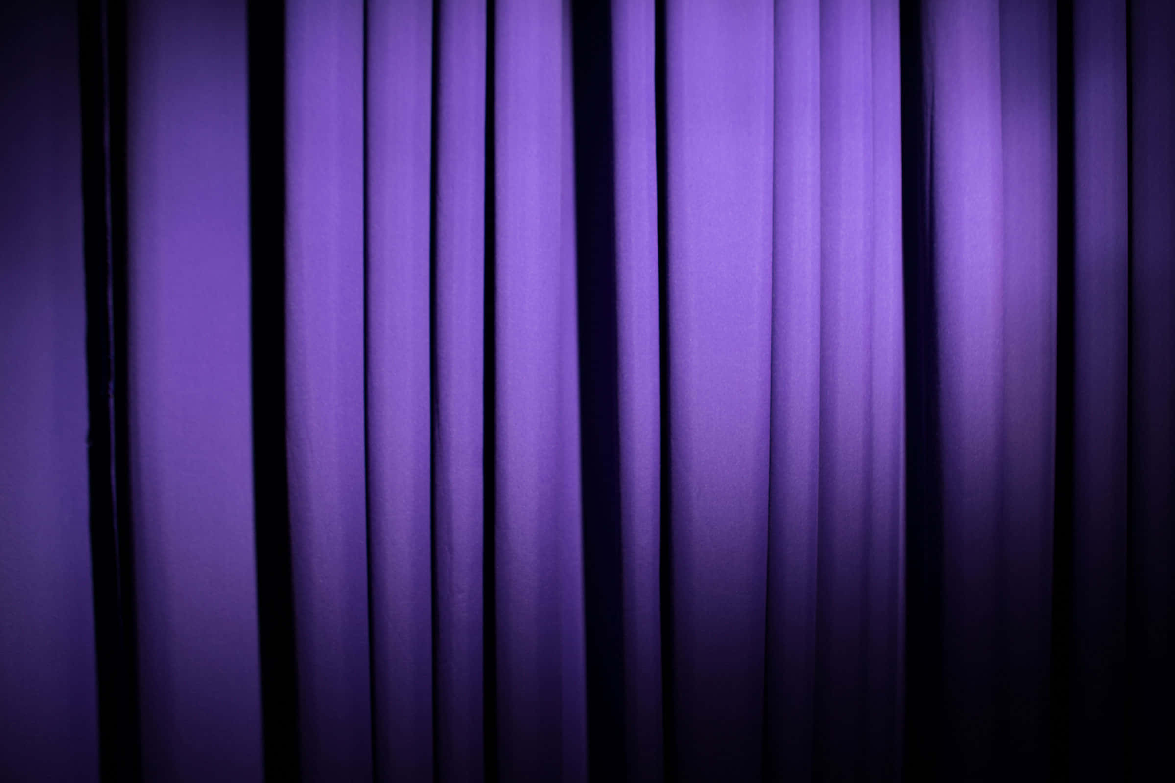 Purple Curtains 桌布 壁紙 — 深紫色嘅劇院窗簾以柔軟嘅垂直褶皺懸掛，由背後嘅戲劇性舞台燈光照亮。
