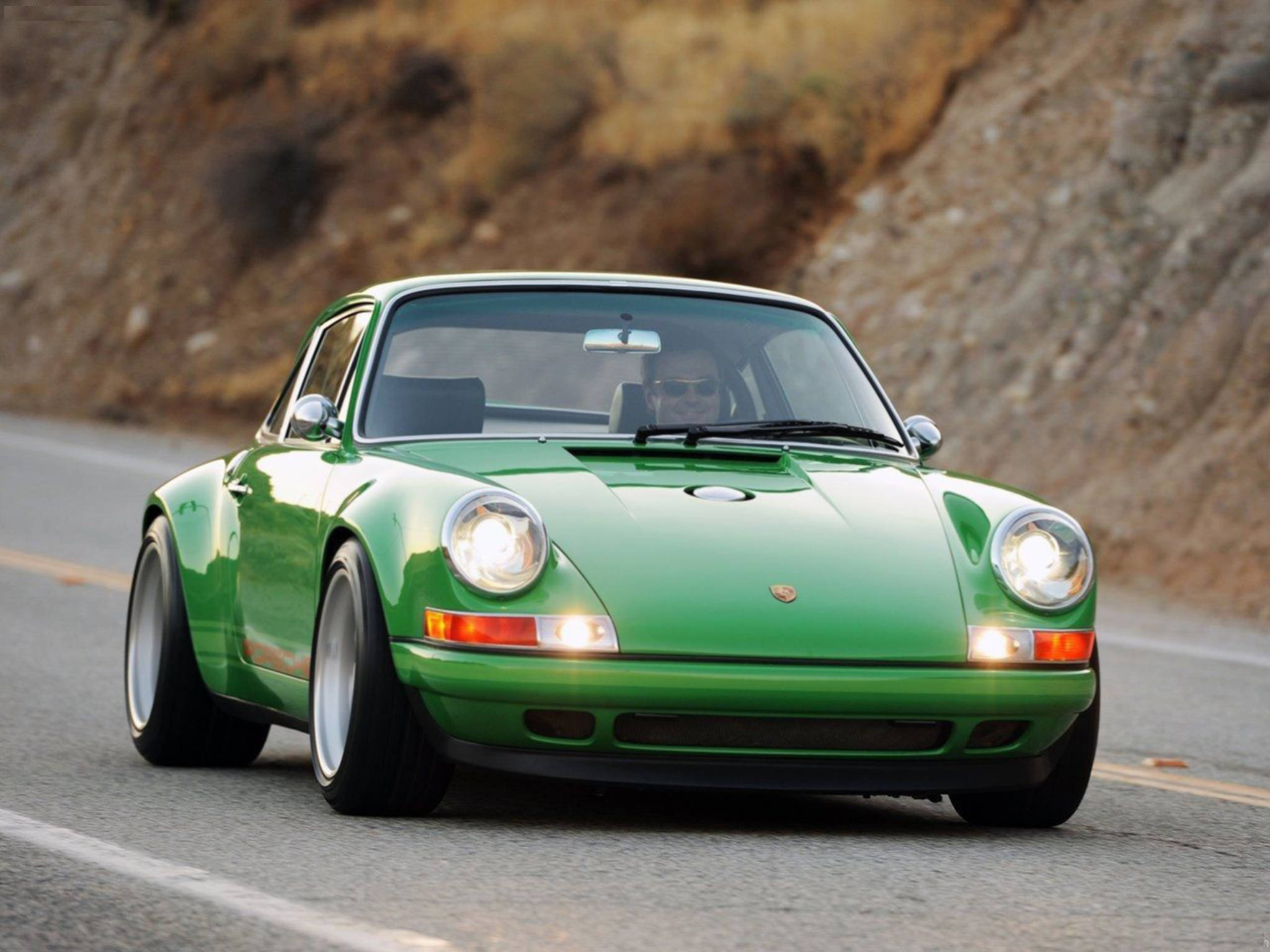 深綠色Singer Porsche 壁紙 — 一輛充滿活力的綠色經典保時捷911在蜿蜒的山路上飛馳，車頭燈閃爍。