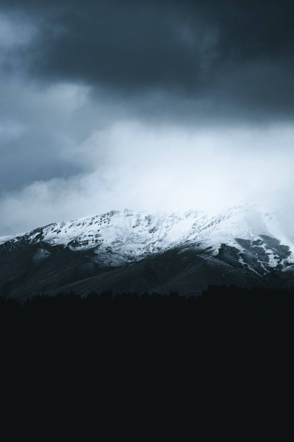 暴風雲下的雪山峰，下方有黑暗的森林