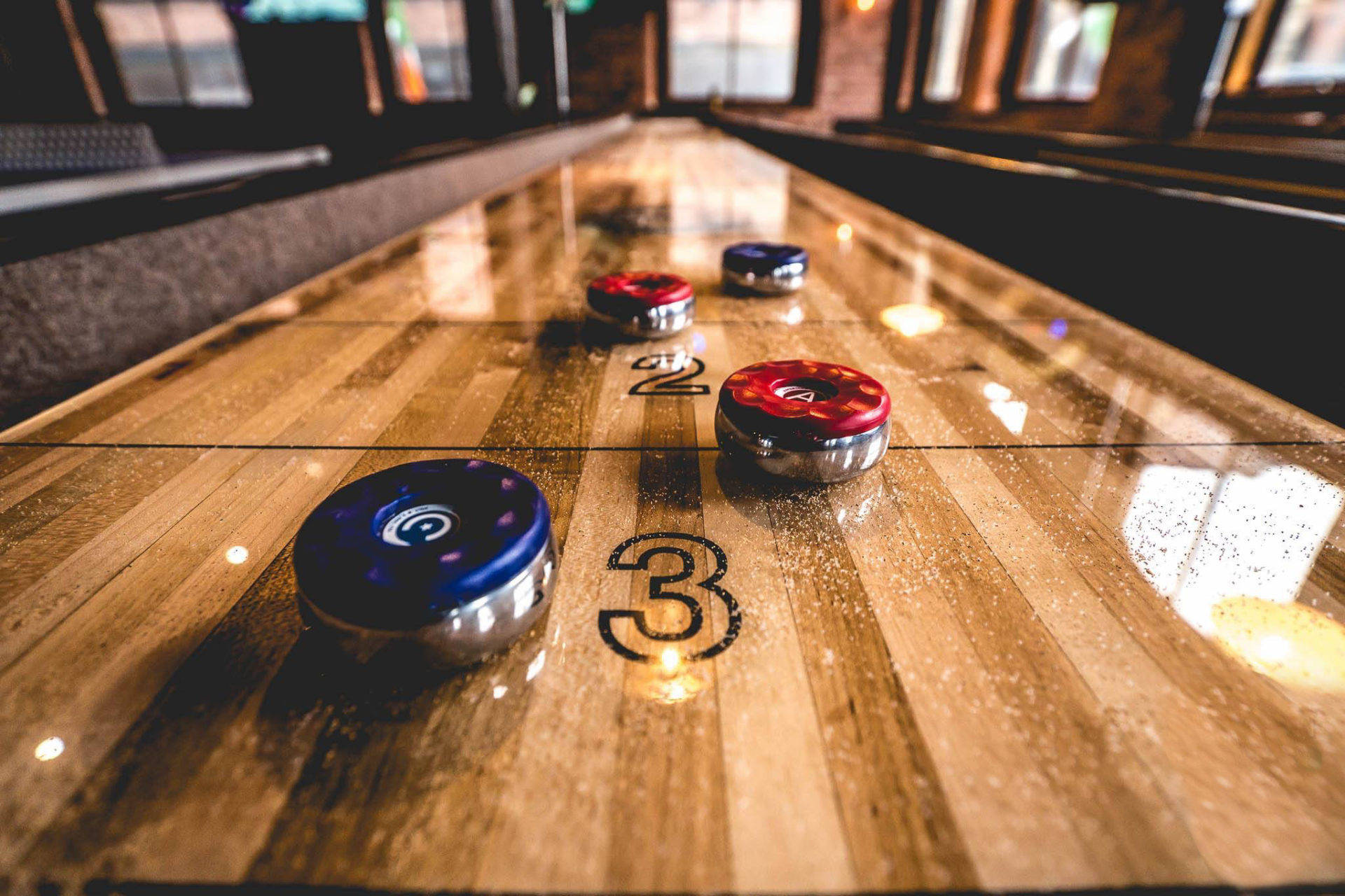深色復古 Shuffleboard 近距離拍攝 壁紙 — 冰壺石在拋光木製賽道上帶有編號賽道和溫暖環境照明的特寫。