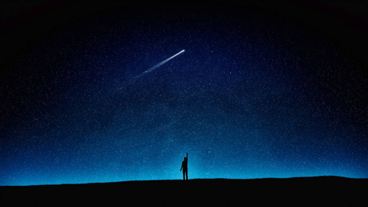 山丘上的人伸手抓向繁星夜空中的彗星
