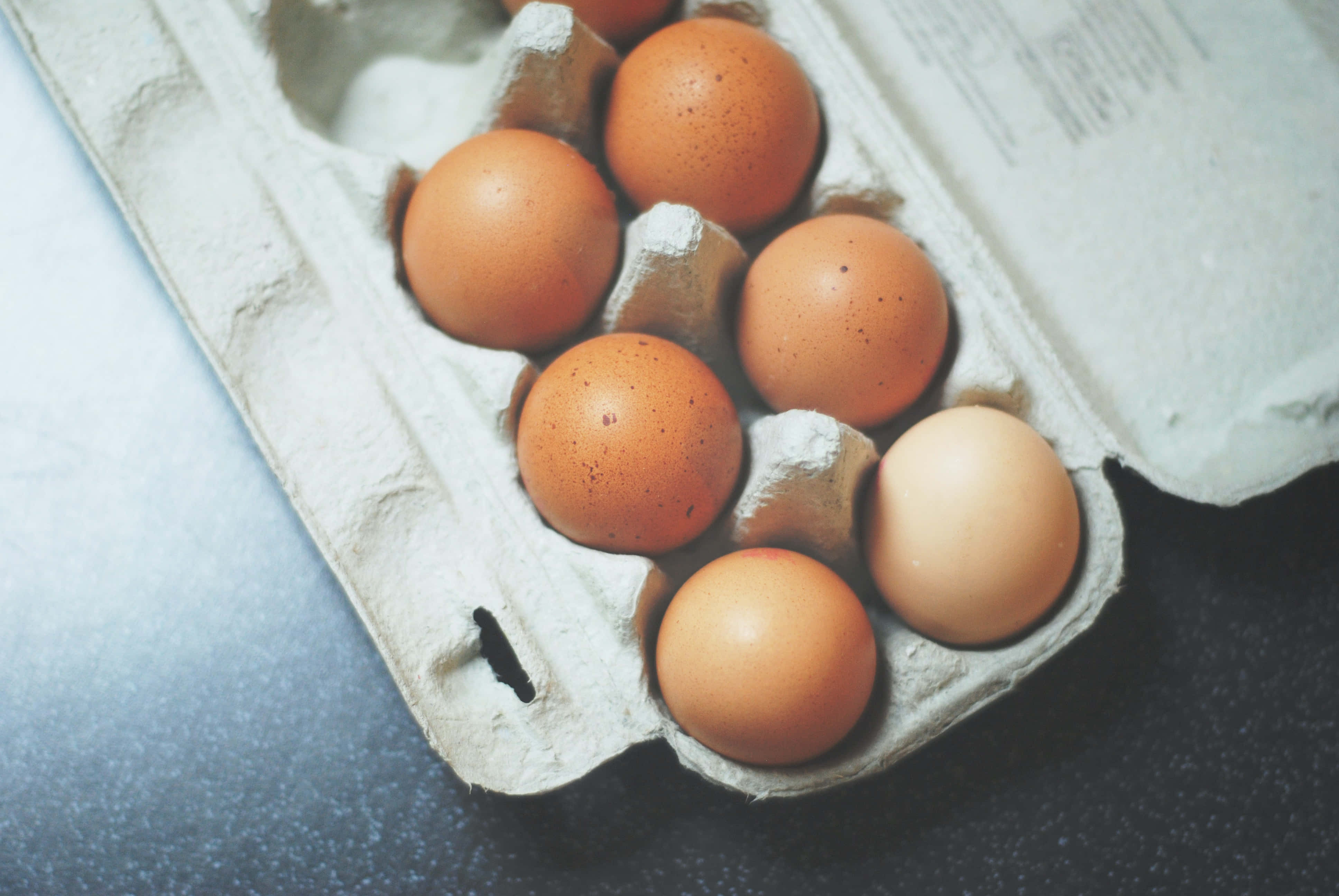 Brown Eggs 桌布 壁紙 — 深色枱面上一個破舊紙盒內嘅棕色雞蛋特寫。