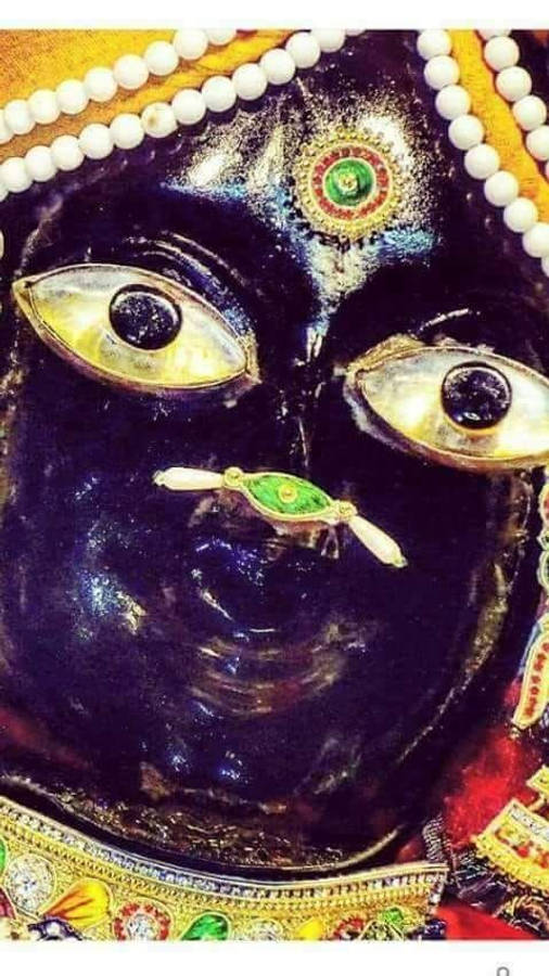 krishna god 桌布 壁紙 — 深色皮膚神祇的特寫，擁有金色眼睛、綠色寶石額飾和飾有複雜金飾的白色珠冠。