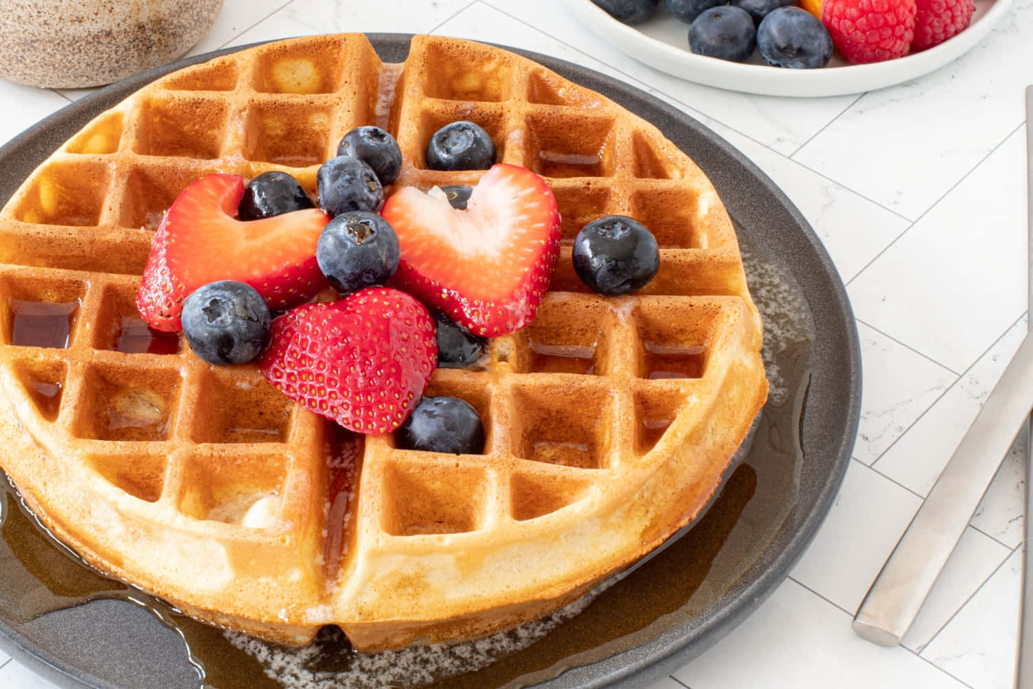 Waffle 桌布 壁紙 — 深色碟上放有金黃色窩夫，配上新鮮士多啤梨、藍莓和糖漿。