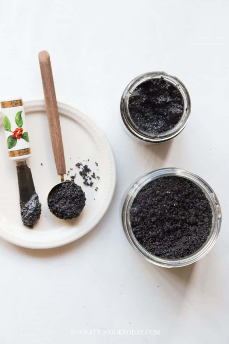 Black Sesame 桌布 壁紙 — 深色粗黑糖磨砂膏裝在玻璃罐中，配木勺放在白色碟上，俯拍鏡頭。