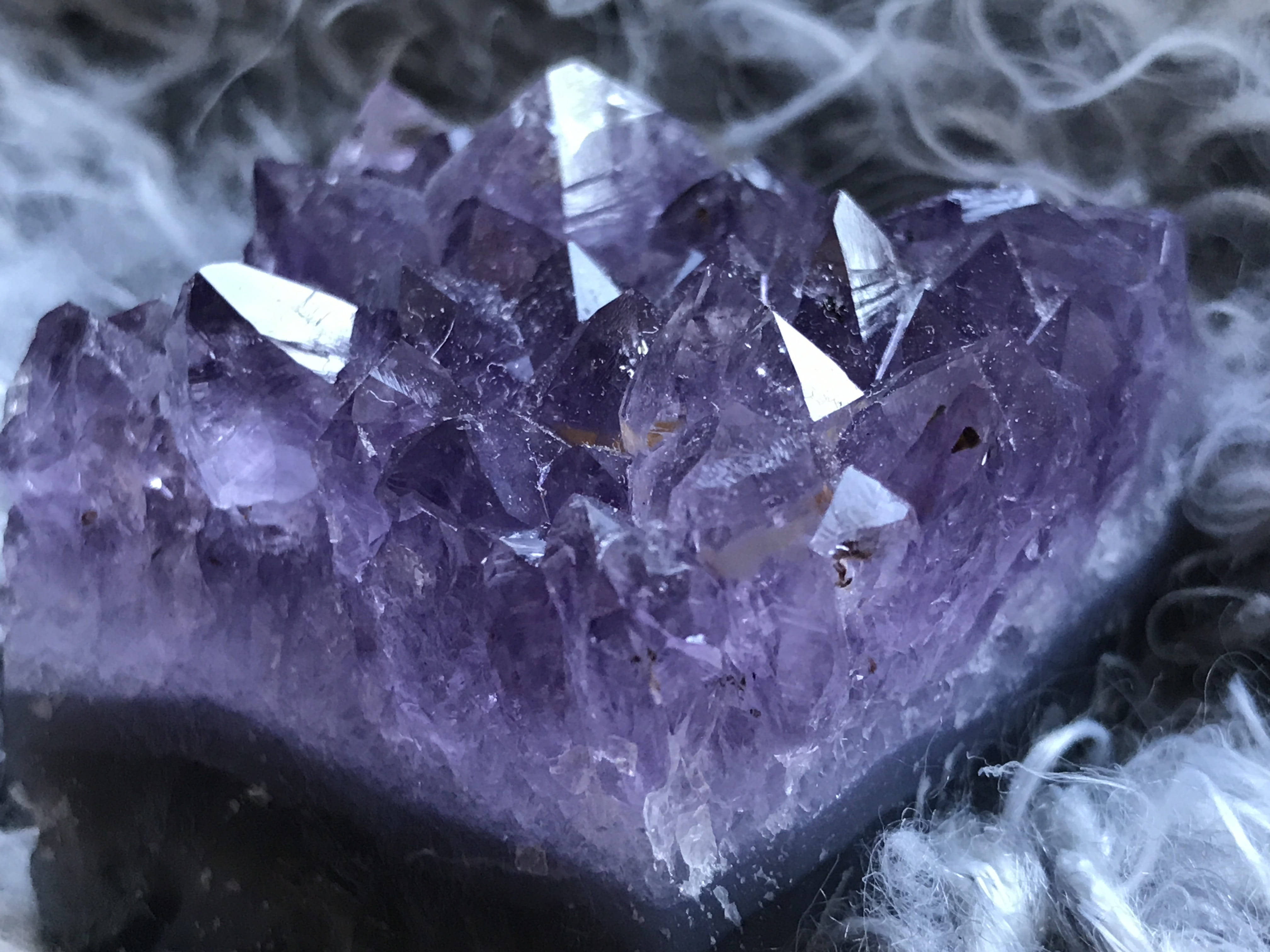 深色紫水晶碎片 壁紙 — 一組閃閃發光的紫色紫水晶晶體簇的特寫，周圍環繞著旋轉的白煙。