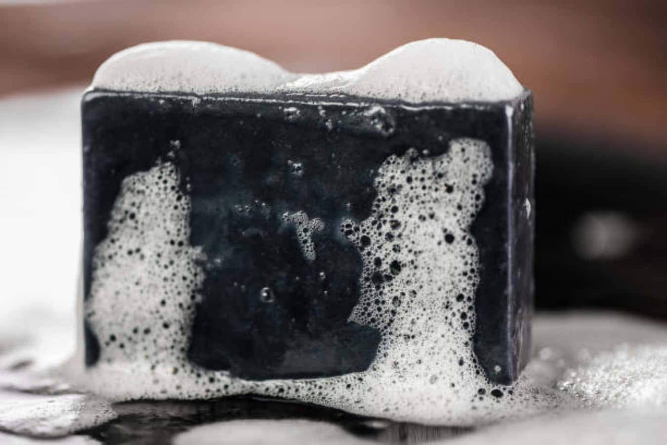 Black Soap 桌布 壁紙 — 深色肥皂塊的特寫，表面形成豐富的白色泡沫並沿側面滴落。