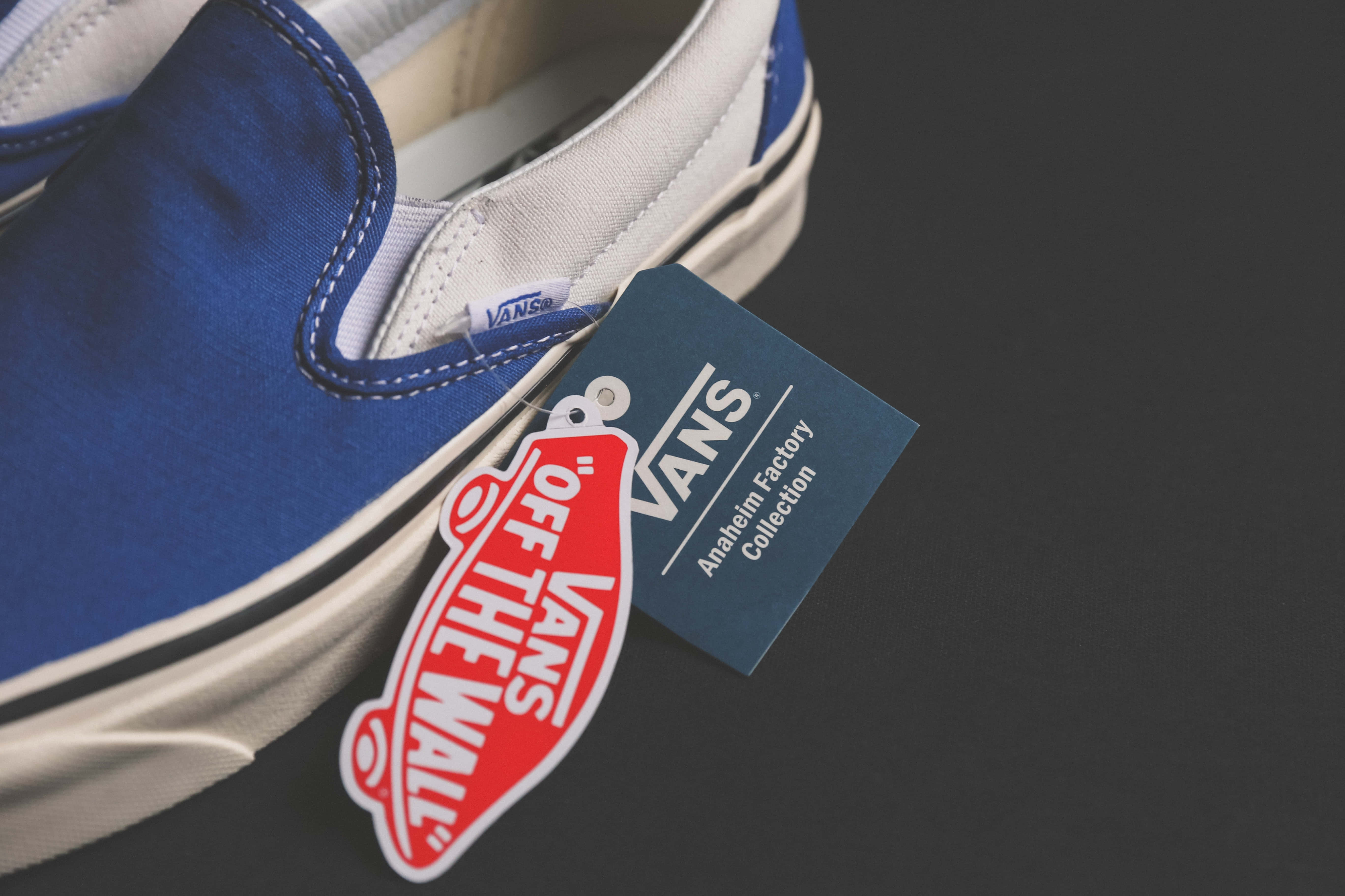 Navy Blue Shoes 桌布 壁紙 — 深色背景上，一雙帶有白色縫線及附有品牌標籤的藍色Vans slip-on運動鞋特寫。