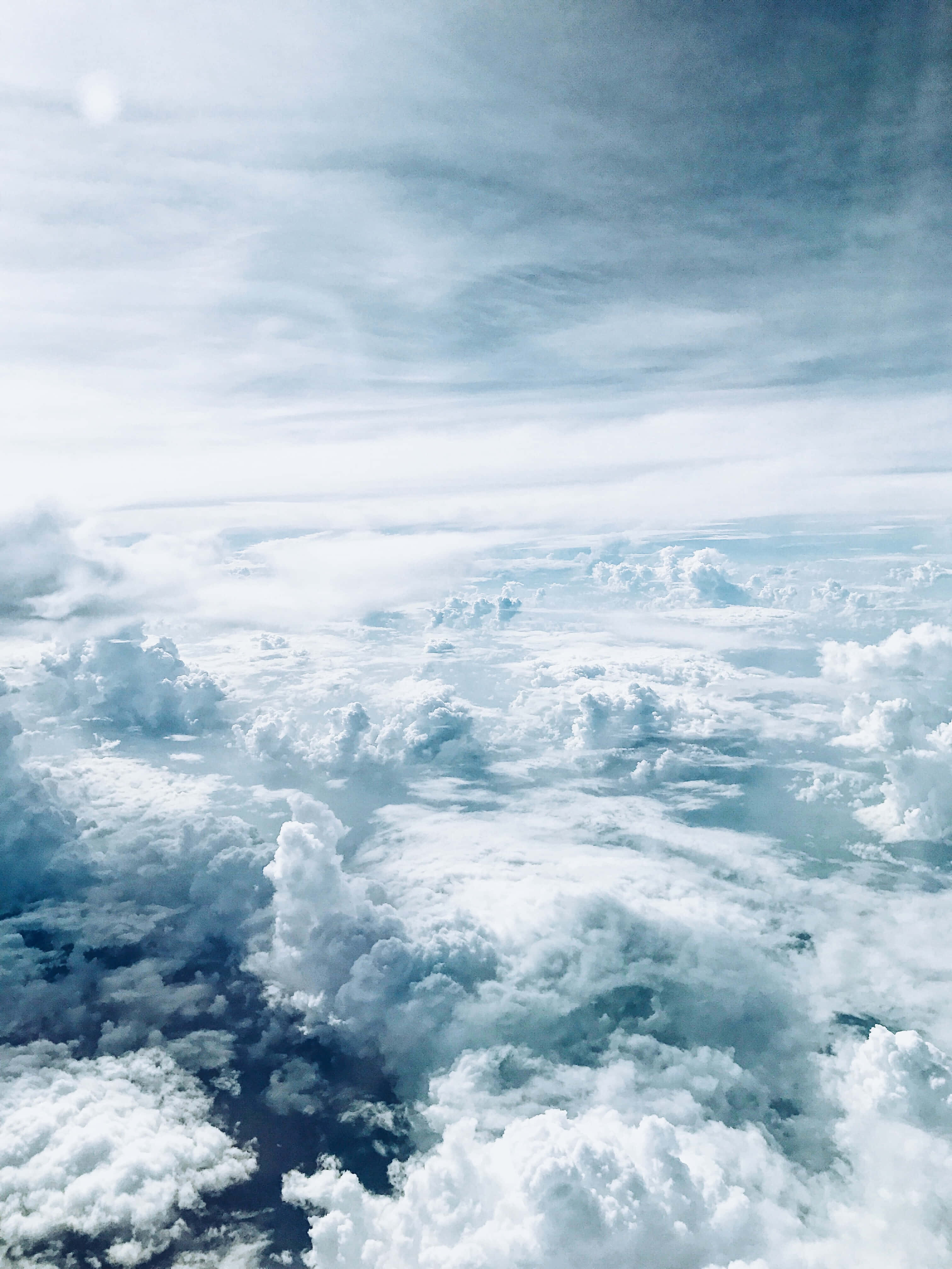 深色背景上的天堂雲朵 壁紙 — 從高空俯瞰，柔軟的白雲在淡藍色天空下無盡延伸，上方有縷縷卷雲。