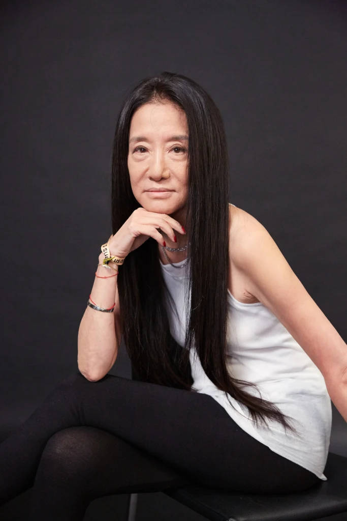 一位長黑髮的女士在攝影棚裡穿著白色上衣和黑色緊身褲靜靜地坐著。