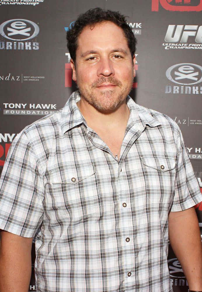 Jon Favreau 桌布 壁紙 — 深色頭髮和鬍鬚的男子在UFC活動背景下穿著格仔恤衫。