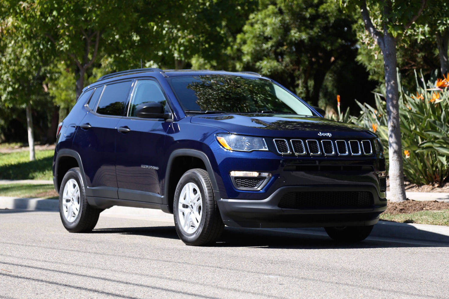 藍色Jeep Compass SUV停泊在陽光明媚的街道上，有綠色樹木和花朵。
