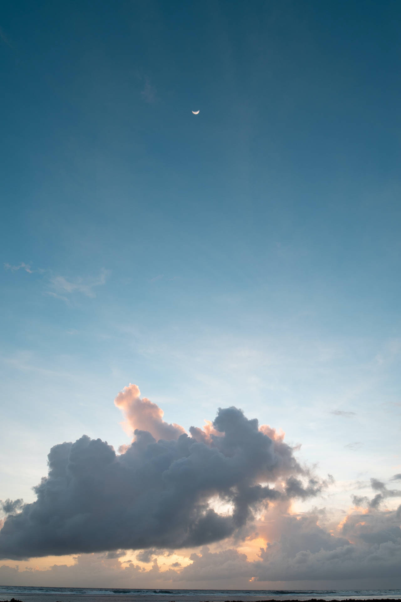 海洋上空日落時分，粉紅雲朵上方的新月。