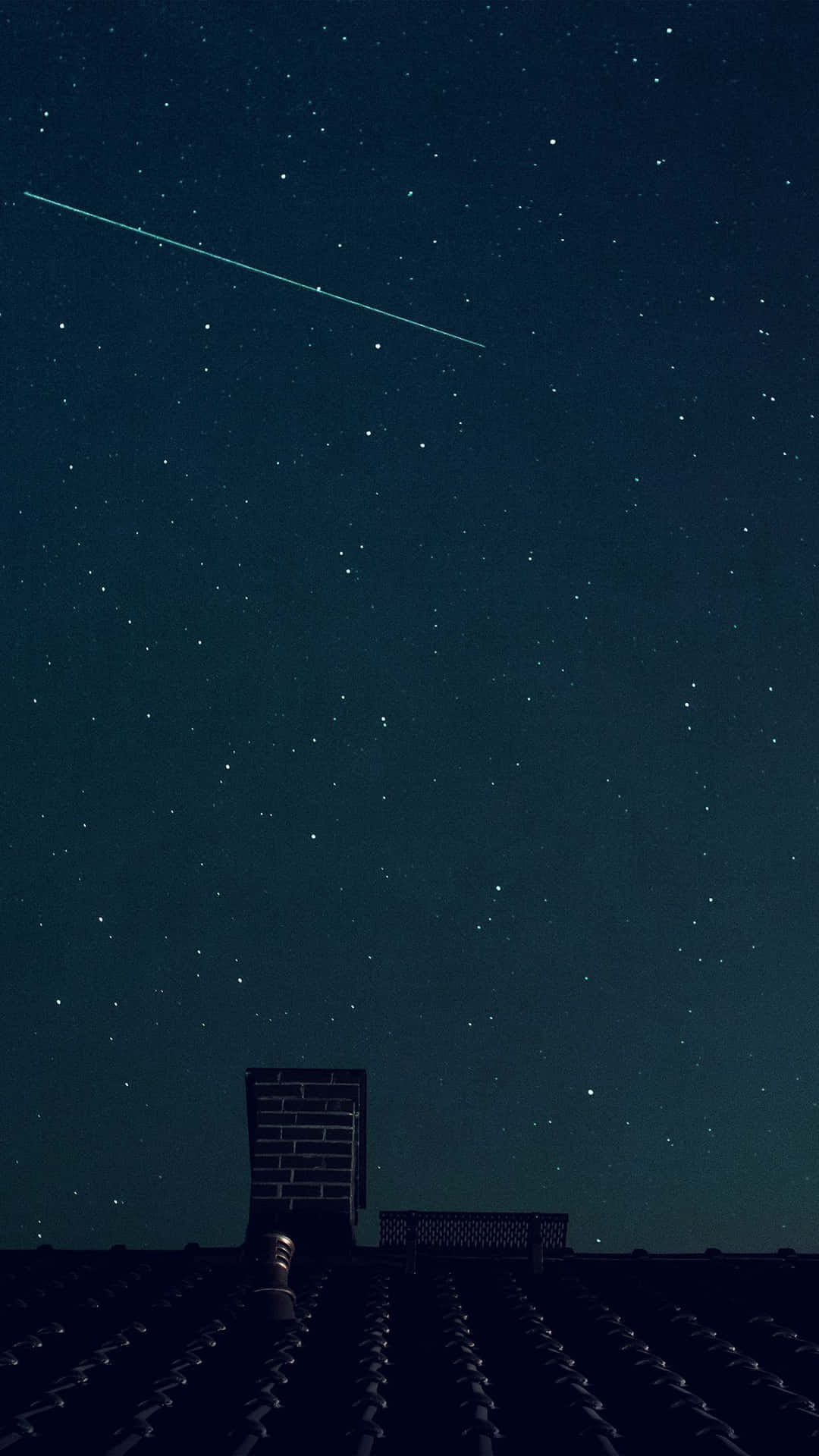 一顆流星劃過屋頂和煙囪上方的繁星夜空。