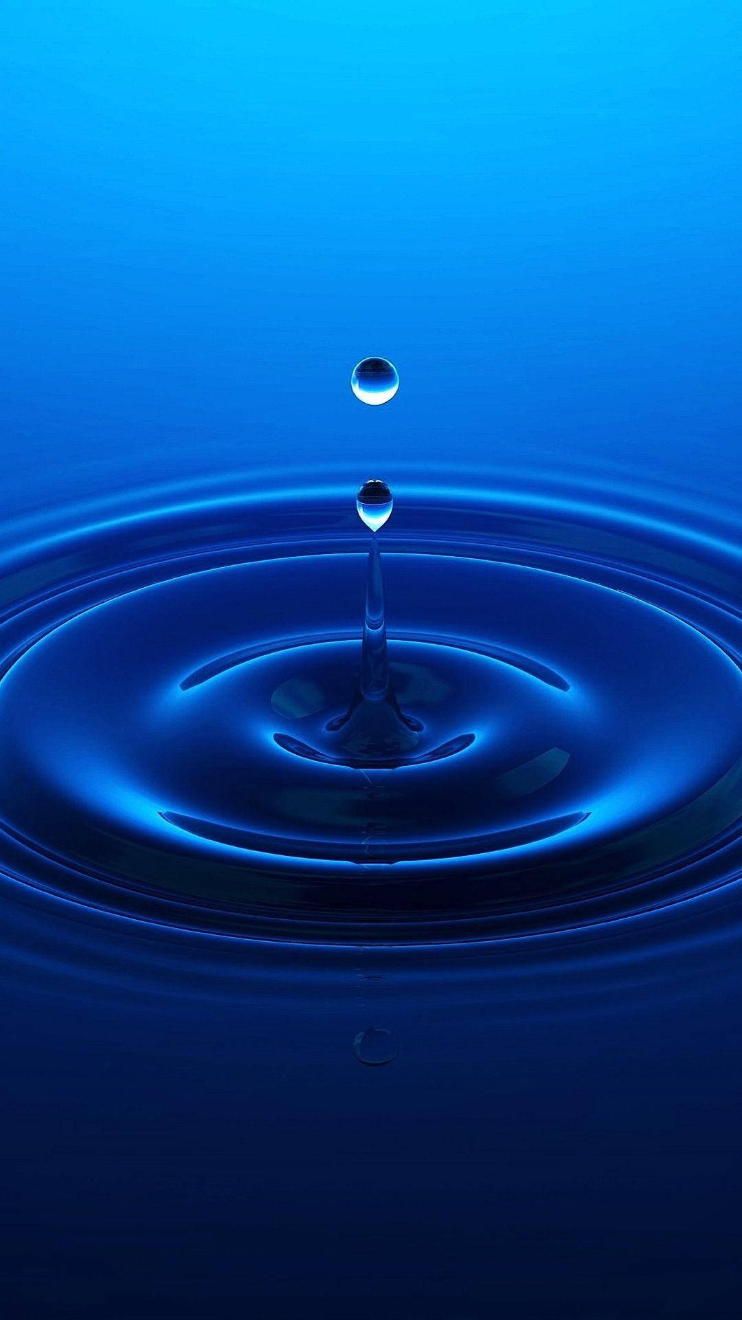 一滴水懸浮在深藍色水面上同心漣漪之上。