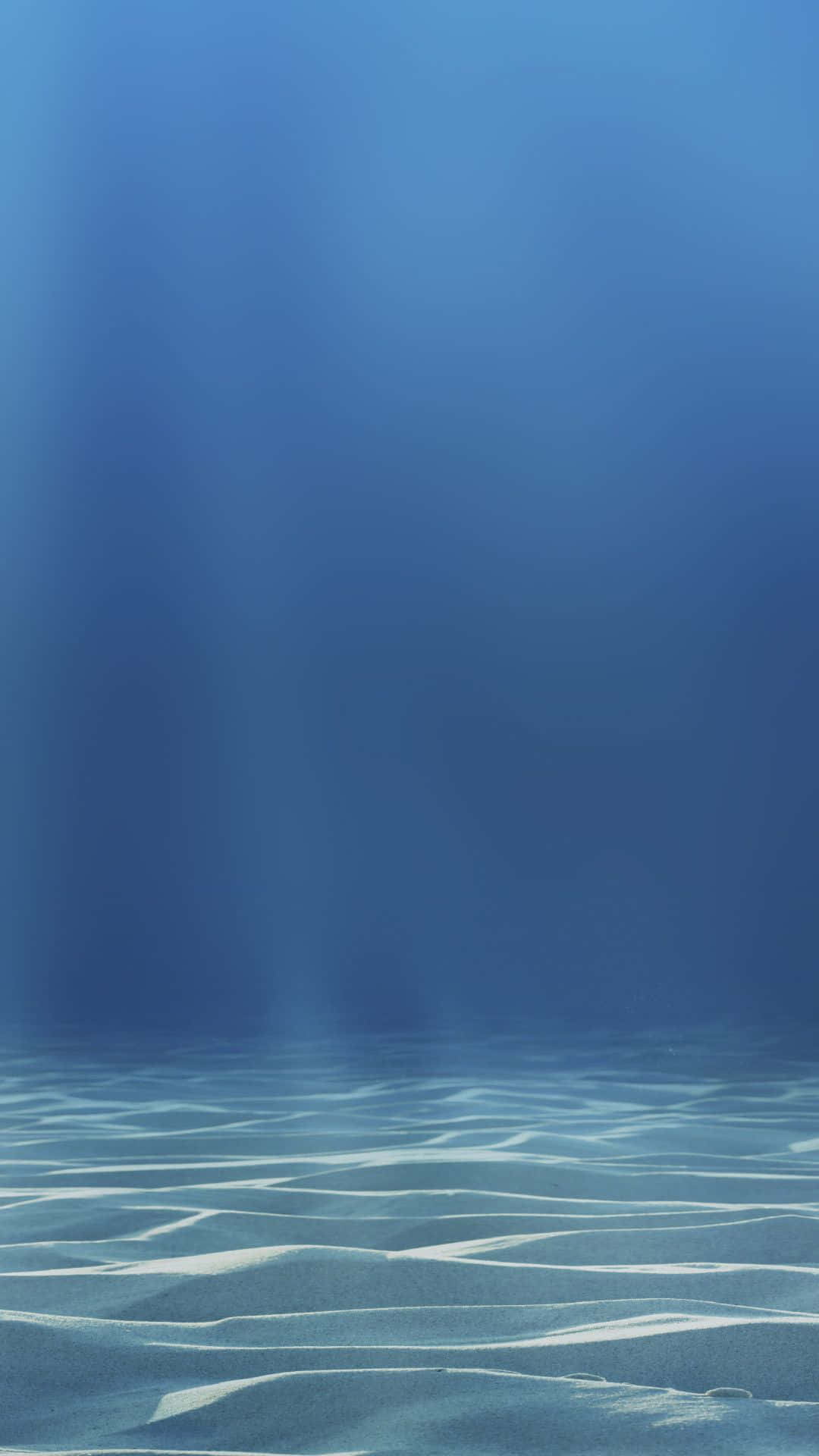 陽光穿過海水照射在波光粼粼的沙質海底上。