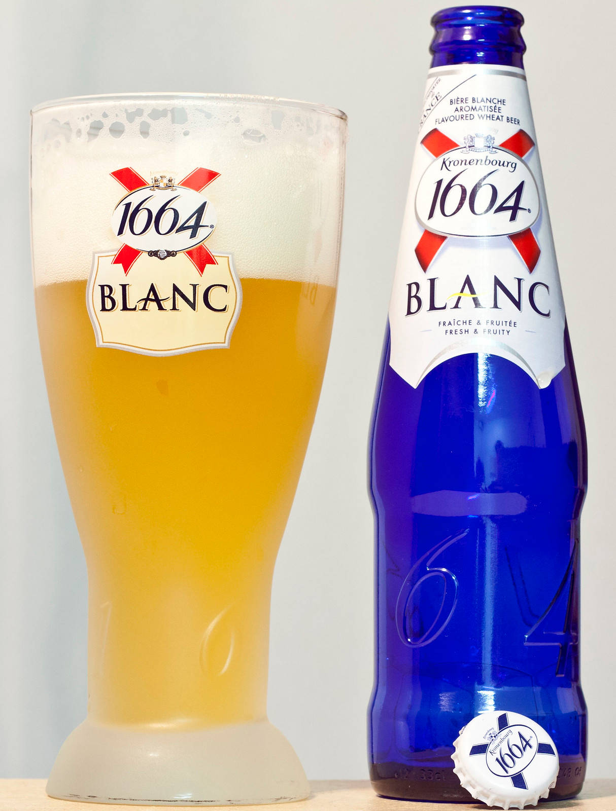 藍色Kronenbourg 1664 Blanc啤酒瓶和玻璃杯，內有金色啤酒和泡沫。