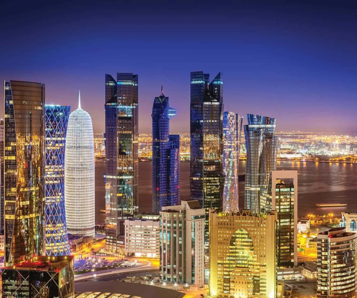 Qatar 桌布 壁紙 — 深藍色天空下，現代摩天大樓閃爍的窗戶倒映在水面上的迷人夜景。