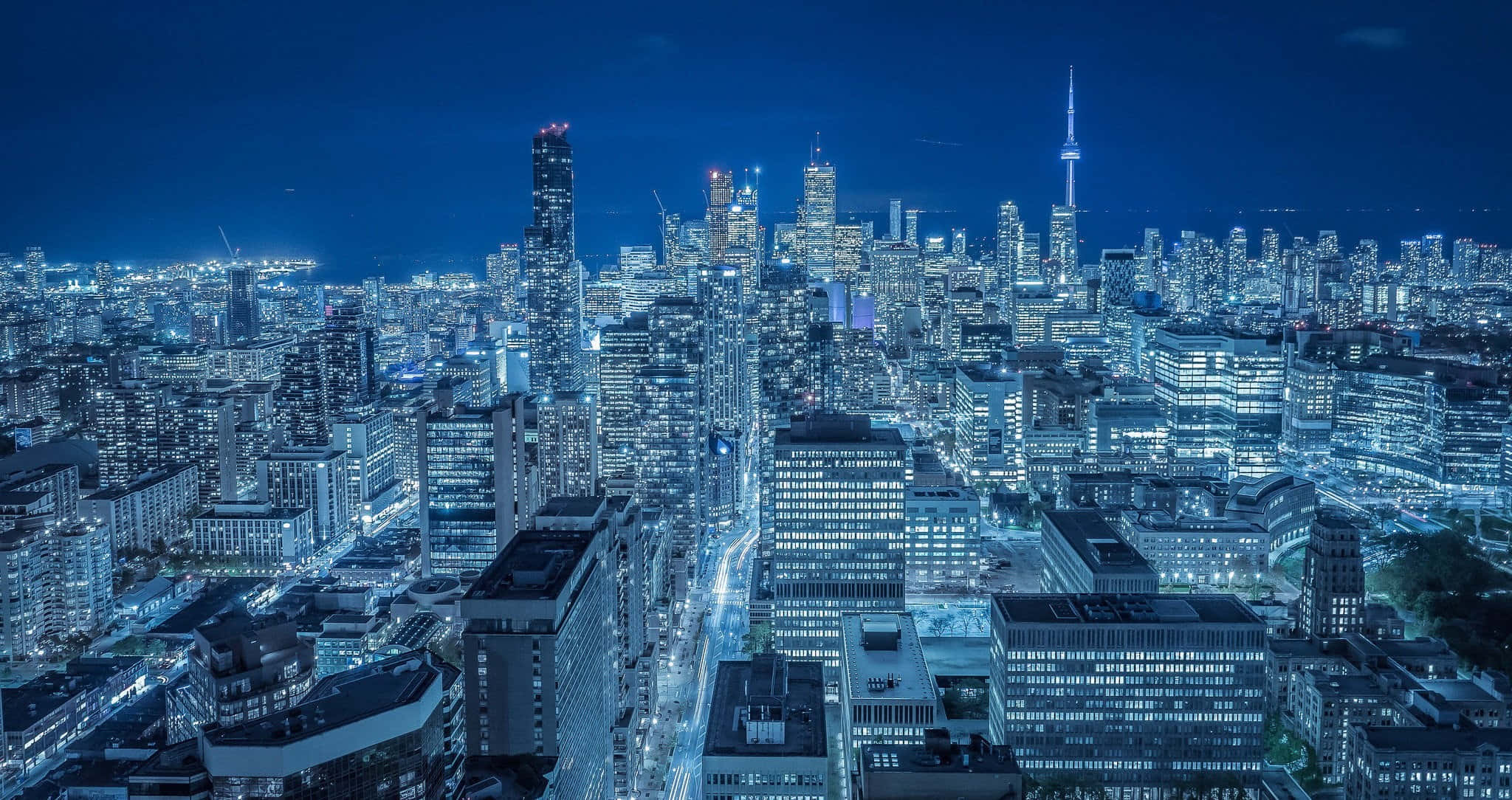 Toronto 桌布 壁紙 — 深藍色天空下，閃爍的摩天大樓和燈火通明的街道構成的廣闊城市夜景鳥瞰圖。