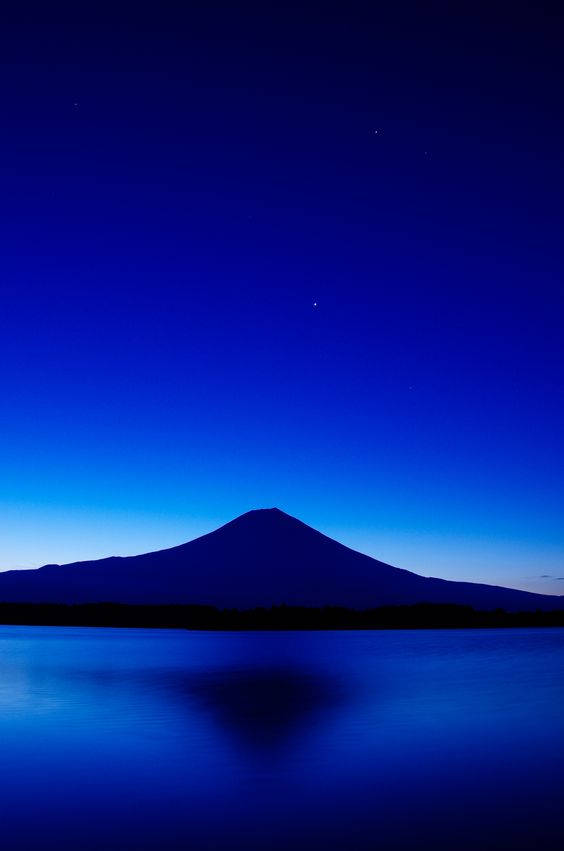 在星光閃爍的暮色天空下，富士山剪影倒映在湖中。