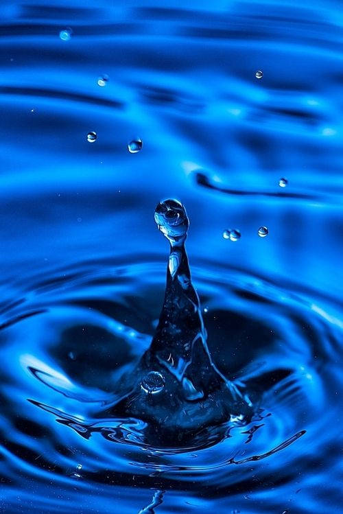 一滴水在深藍色水中向上濺起，形成漣漪和氣泡。