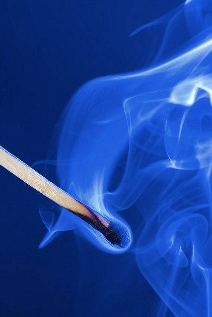 一根點燃的火柴，在深藍色背景下升起藍色煙霧。