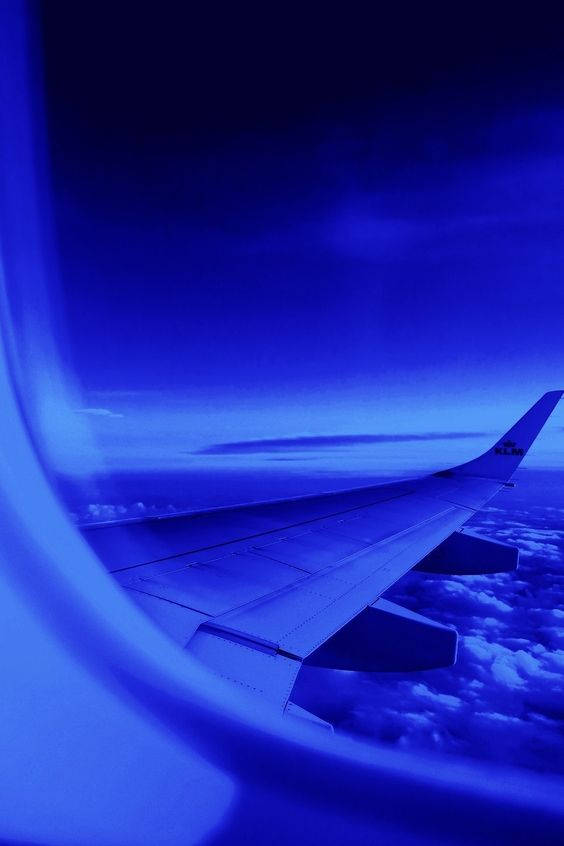 暮色中從窗戶看到雲層上方的飛機機翼。