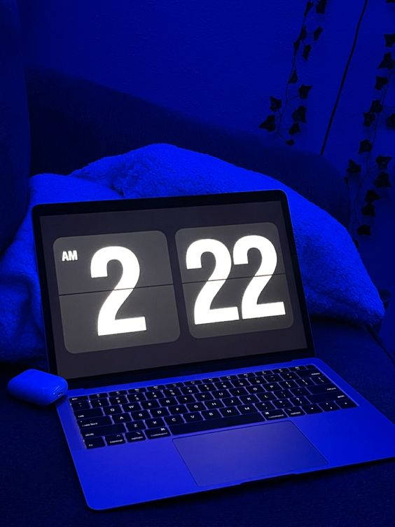 在昏暗的藍色房間的沙發上顯示凌晨2:22的手提電腦。