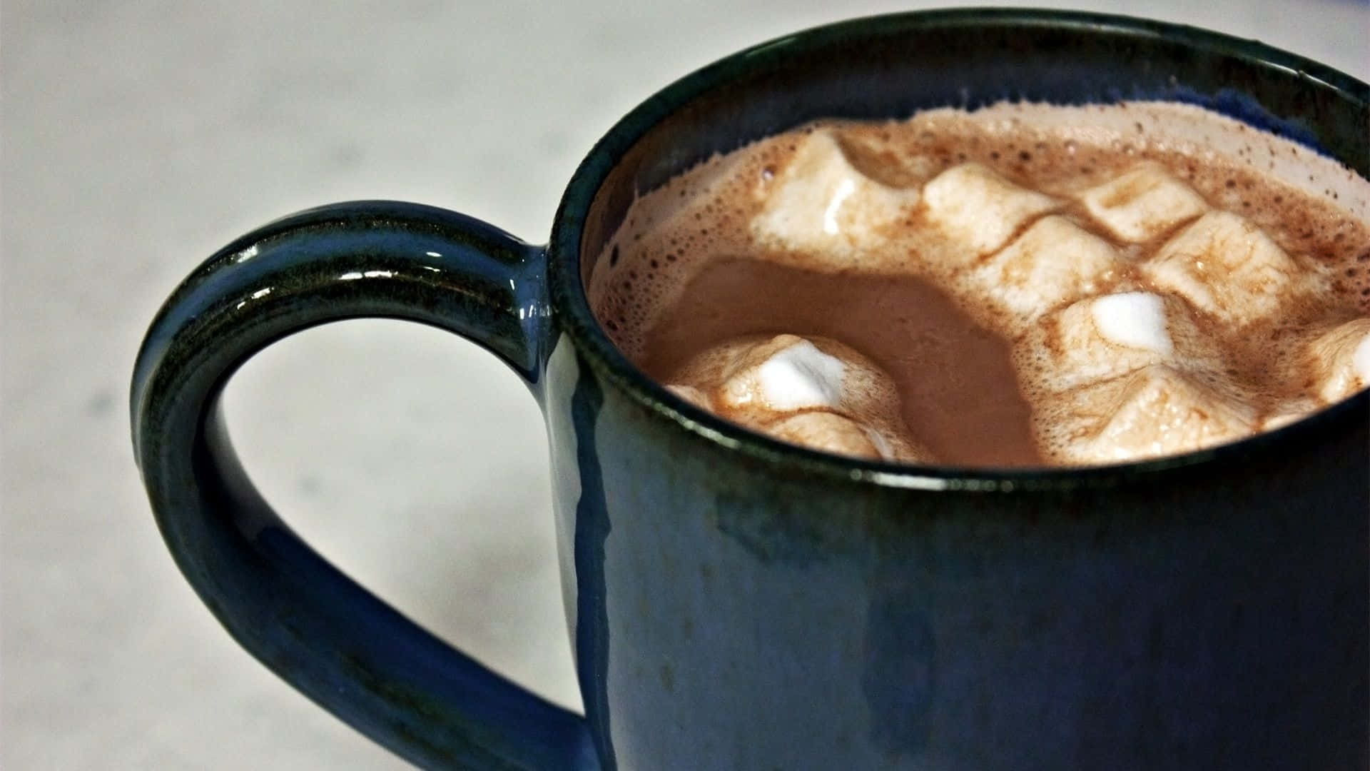 Hot Chocolate 桌布 壁紙 — 深藍色陶瓷杯的特寫，裝滿冒著熱氣的熱朱古力，上面放著鬆軟的白色棉花糖。