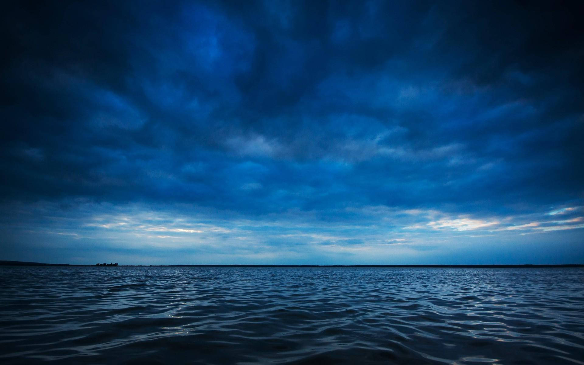 深藍調寧靜海面 壁紙 — 廣闊的深藍色湖泊，在暴風雨黃昏的天空下，有戲劇性的雲層形成。