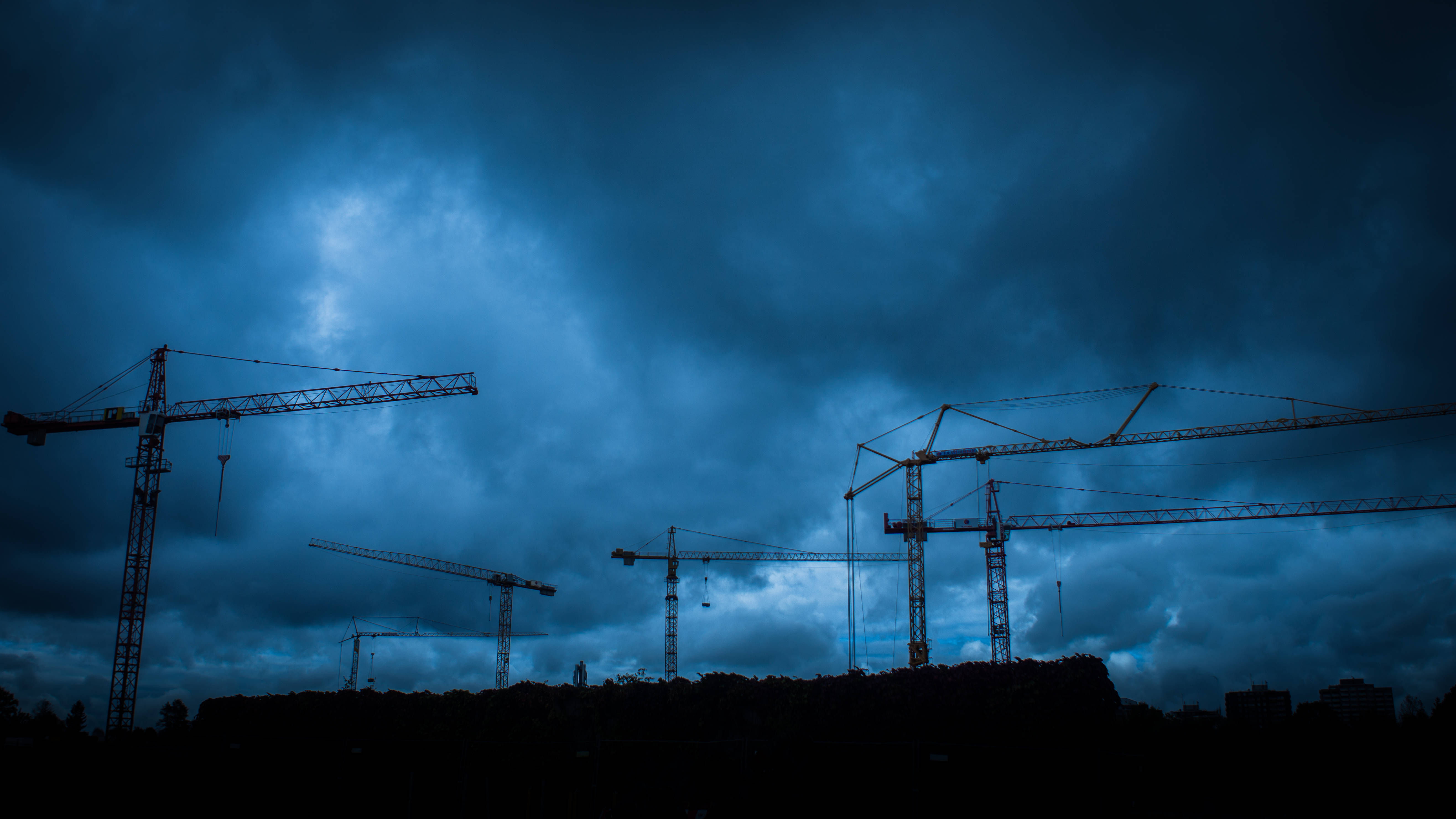 深藍雲層 壁紙 — 建築起重機的剪影在黃昏時分，與陰鬱的電藍色暴風雨天空形成鮮明對比。