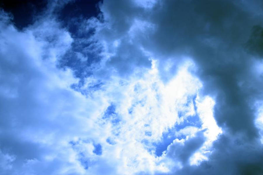 深藍雲層與陽光穿透 壁紙 — 戲劇性的藍色雲朵圍繞著一道明亮的陽光，穿透暴風雨的天空。