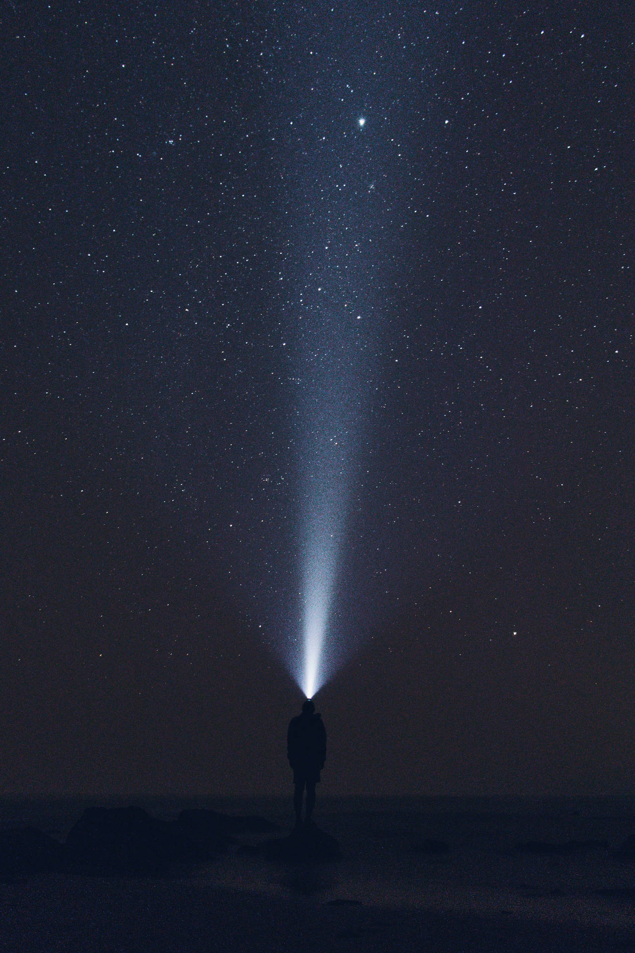 人站在岩石上將手電筒照向星空