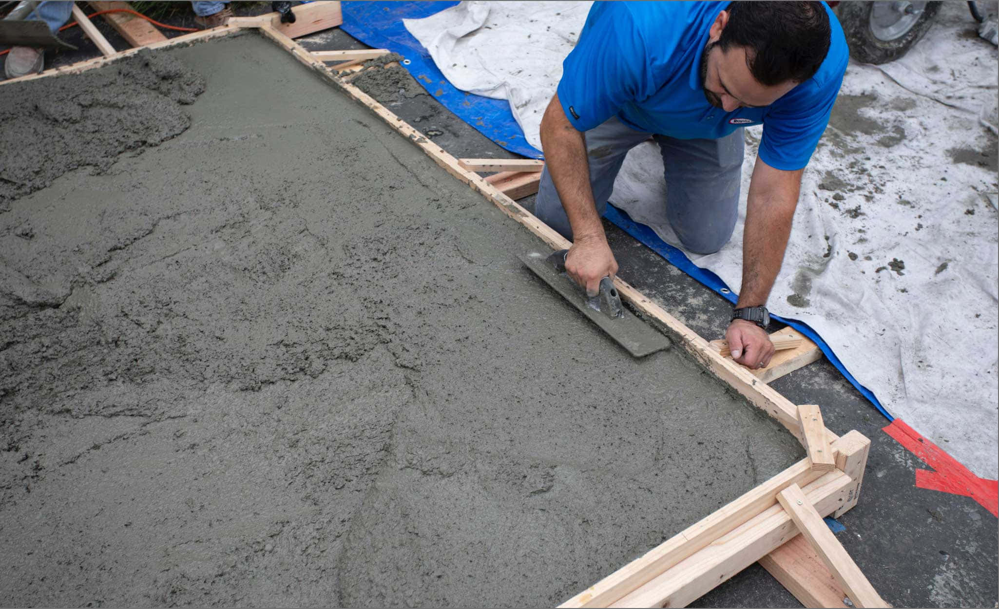 混凝土澆灌圖像 壁紙 — 一名身穿藍色襯衫的建築工人在雪地上小心地將木模板內的濕混凝土抹平。