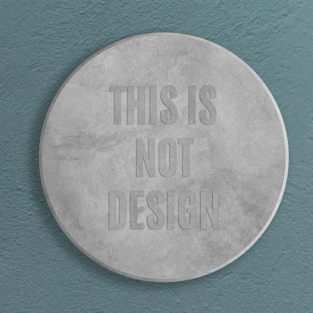 混凝土硬幣景觀 壁紙 — 一個圓形混凝土牌，上面有浮雕文字 'THIS IS NOT DESIGN'，安裝在帶紋理的青綠色牆上。