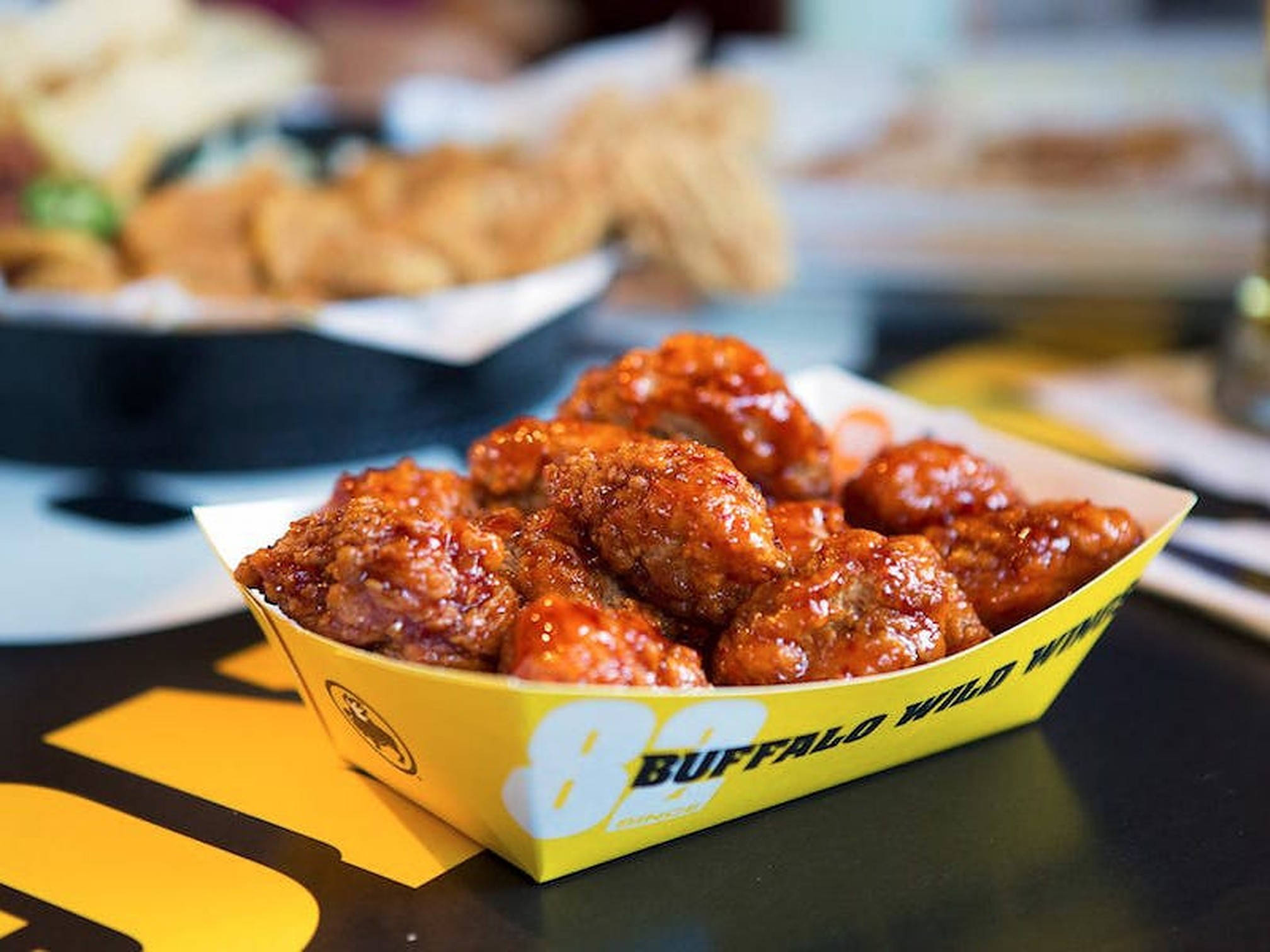 淺景深 Buffalo Wild Wings 壁紙 — 脆皮水牛城雞翼在黃色Buffalo Wild Wings紙托盤中閃耀著鮮紅色的醬汁。